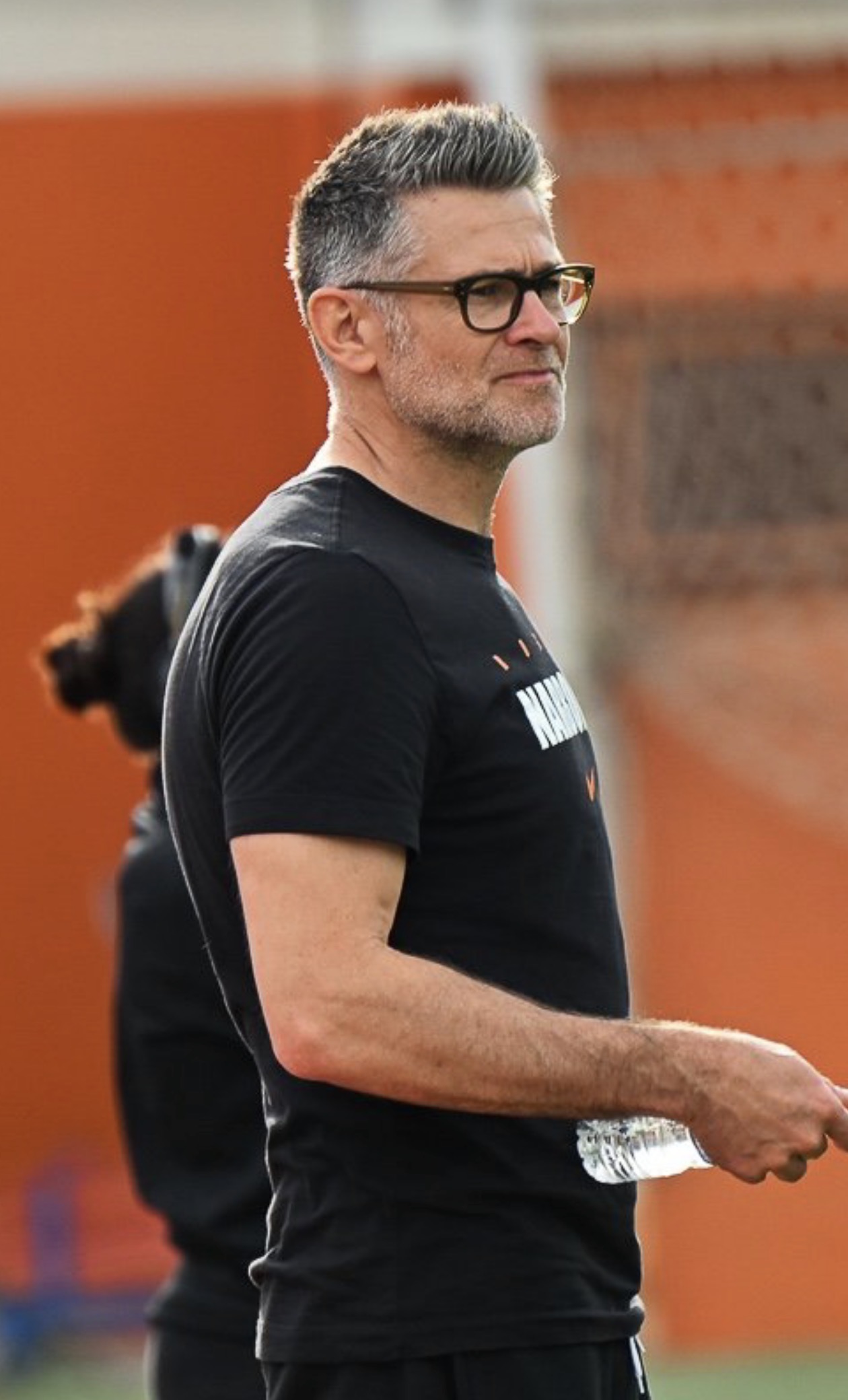 Nicolas Roger de profil sur le terrain, fond orange